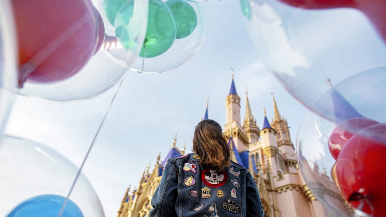 Staying at any of the best Disney deluxe resorts in Walt Disney World will having you feeling like this girl - surrounded by Mickey balloons, decked out in her favorite Disney jacket, and spending her time in the castle of her dreams