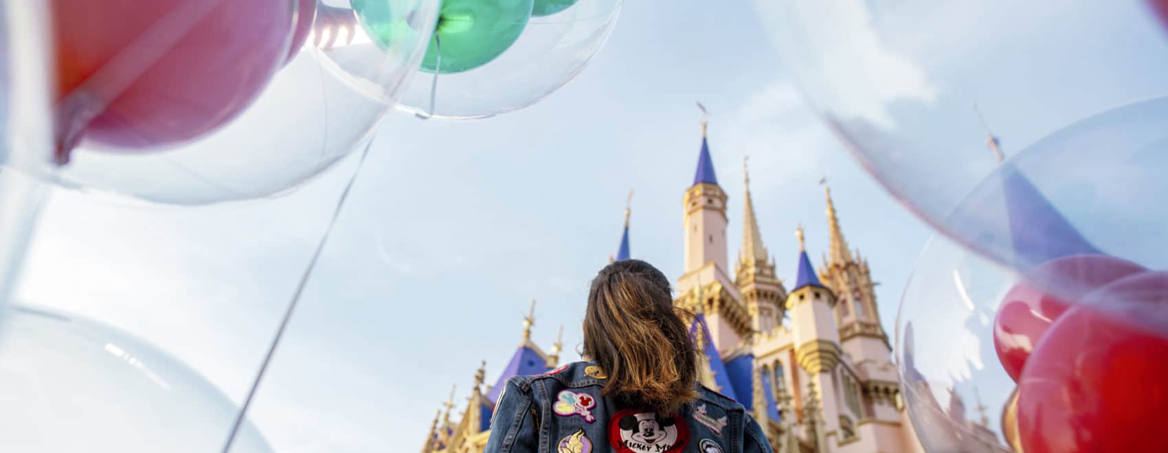 Staying at any of the best Disney deluxe resorts in Walt Disney World will having you feeling like this girl - surrounded by Mickey balloons, decked out in her favorite Disney jacket, and spending her time in the castle of her dreams