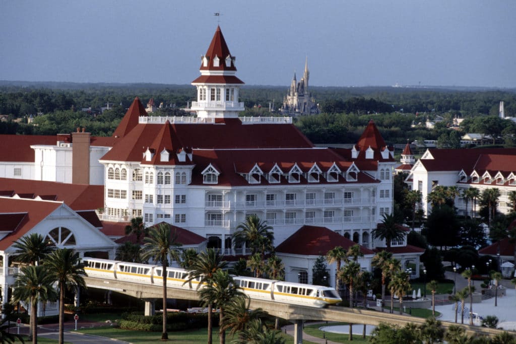 The famous Walt Disney World monorail pulls up to the stunning Grand Floridian Resort & Spa, while the magnificent Magic Kingdom Castle shines in the background.