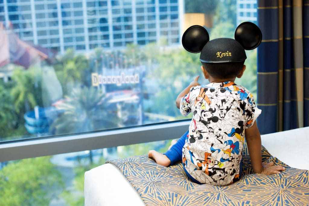 An adorable little boy sports his "Kevin"-monogrammed Mickey ears as he gazes out toward the lovely California views from his bed in the fantastical Disneyland Hotel.