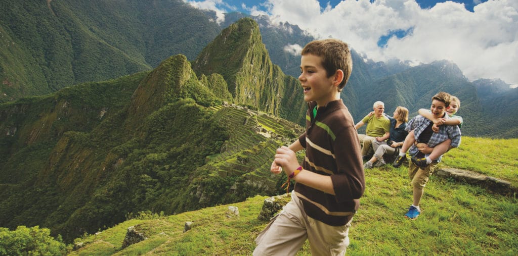 Now you can be as happy as this young boy gazing into the distance and trailed by his piggy-backing siblings plus parents resting on a log in the background, as he gazes at the green wonder and magnificence of Machu Picchu on an Adventures By Disney trip.