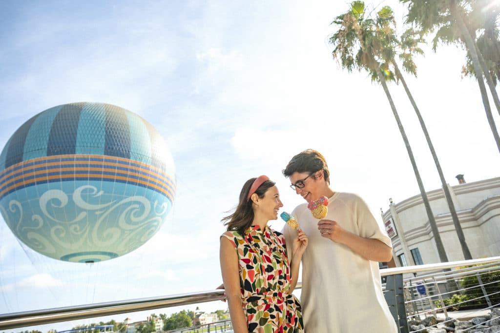 For adults traveling to Disney World, there is so much to see and enjoy - as this young couple is discovering in Disney Springs, with palm trees and hot air balloon rides in the background, plus Mickey Mouse rice crispy treats in their happy hands!