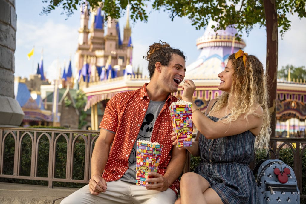 A man and a woman playfully feed each other popcorn on a bench outside of Cinderella's Castle as they enjoy their honeymoon at Disney World