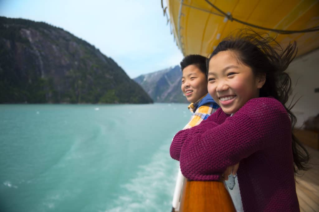 Young brother and sister find common ground enjoying the breeze on the ship deck of their totally-worth-the-cost Disney cruise