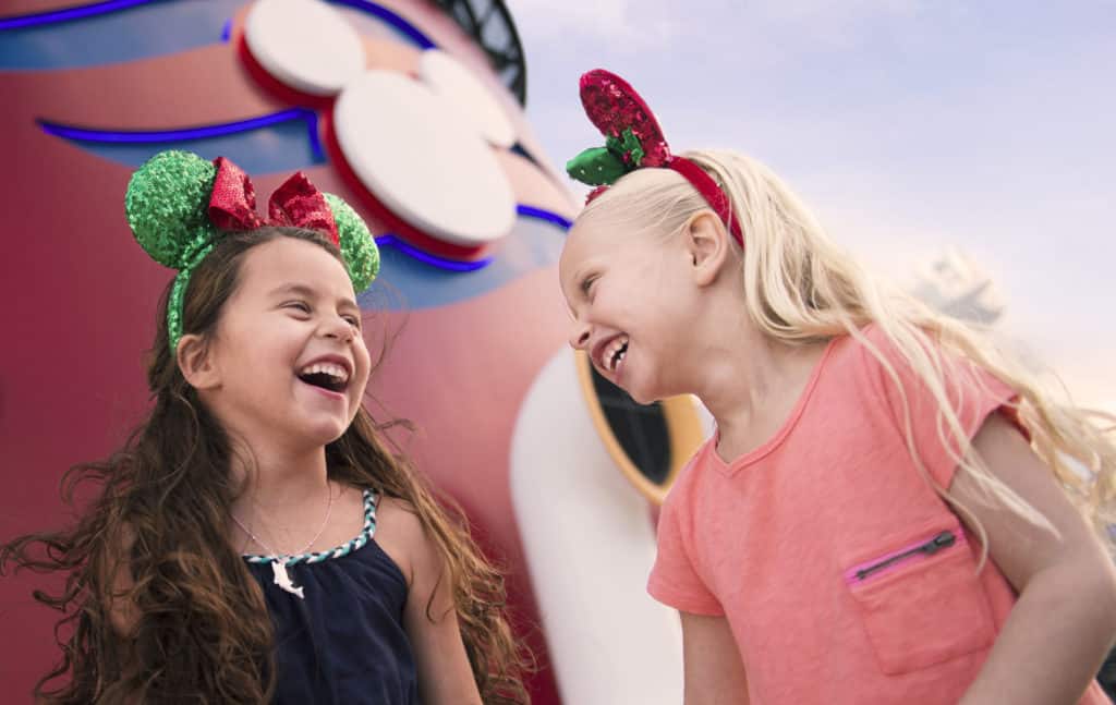 Two young best friends with Christmas Mickey ears laugh on the deck of their Disney Cruise special event: a very merrytime Christmas Disney cruise