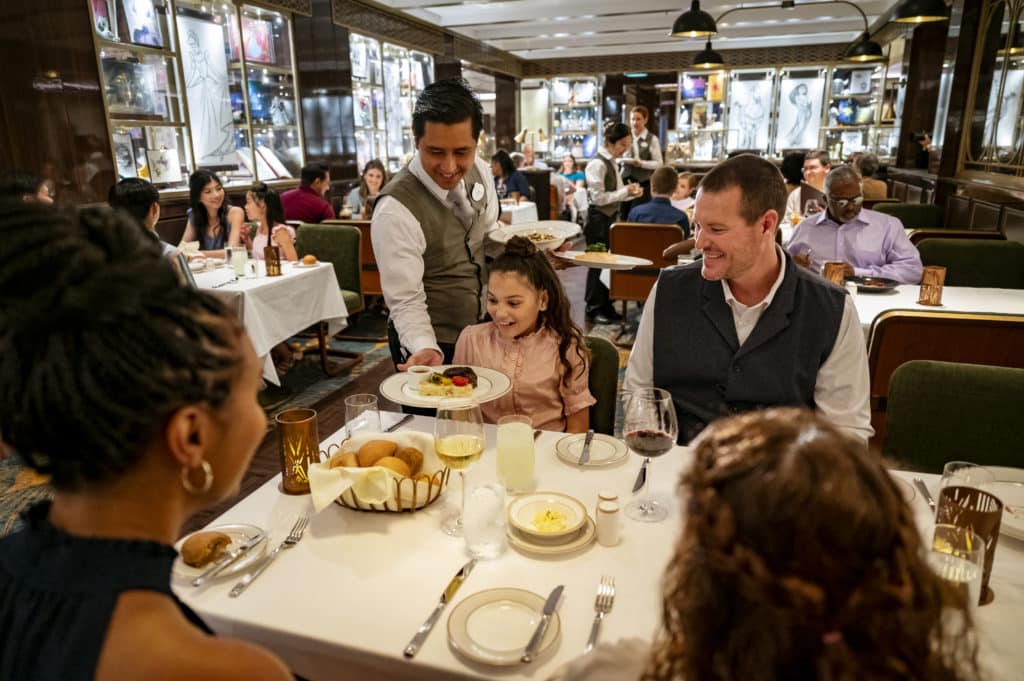 A happy family of four gets served a delicious feast onboard one of the amazing Disney ships in the Disney Cruise Line fleet