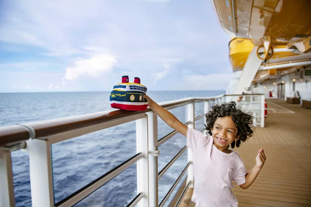 A gleeful kid plays with their stuffed Disney ship on the deck of one of the amazing Disney ships in the Disney Cruise Line fleet.