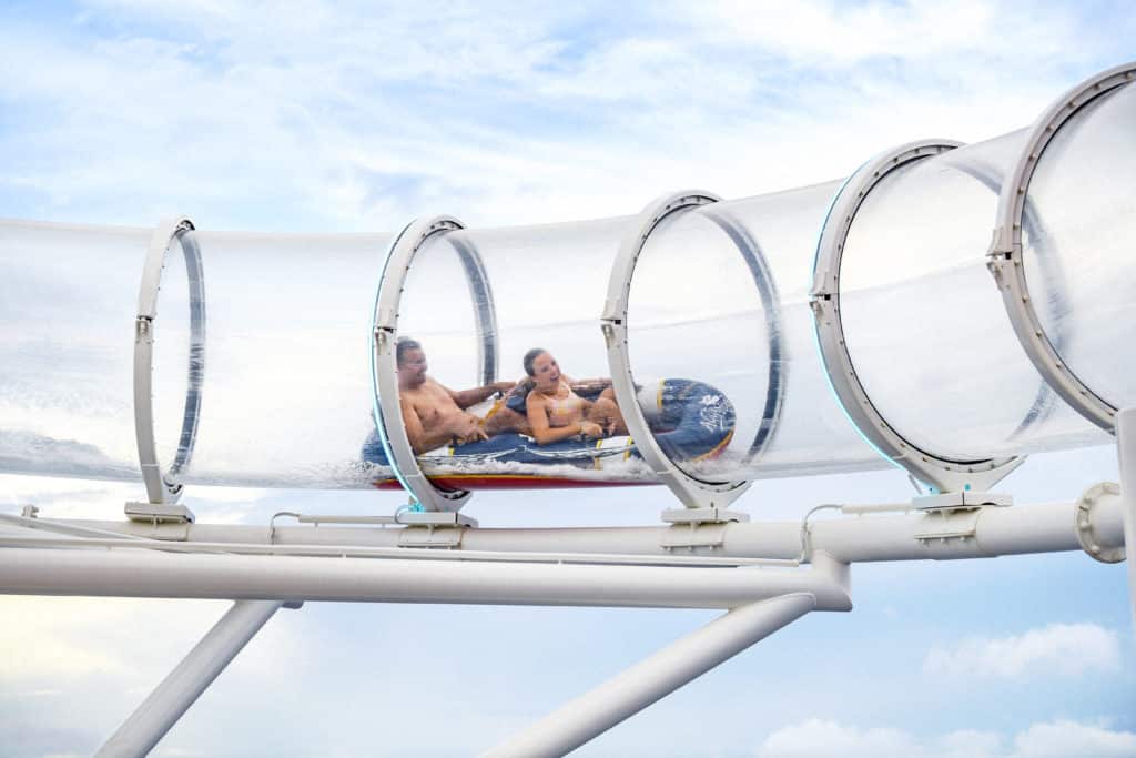 Two delighted adults slide through the transparent AquaDuck suspended high in the air as one of the coolest pools on some of the Disney ships in the Disney Cruise Line fleet