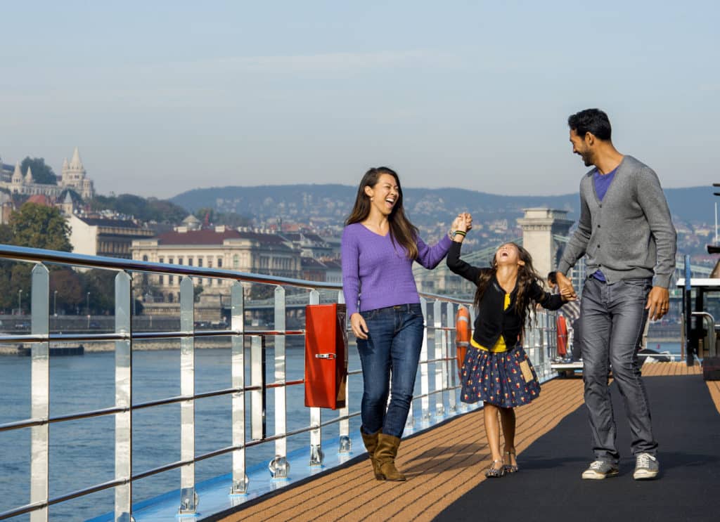 You could be like this laughing family enjoying a Disney River Cruise on the Danube, with a mother and father swinging their daughter along the deck of their cruise ship.